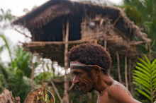 Korowai man in front of traditional treehouse,  West Papua