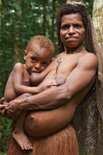 Korowai woman with traditional grass skirt and netbag breastfeeding her kid